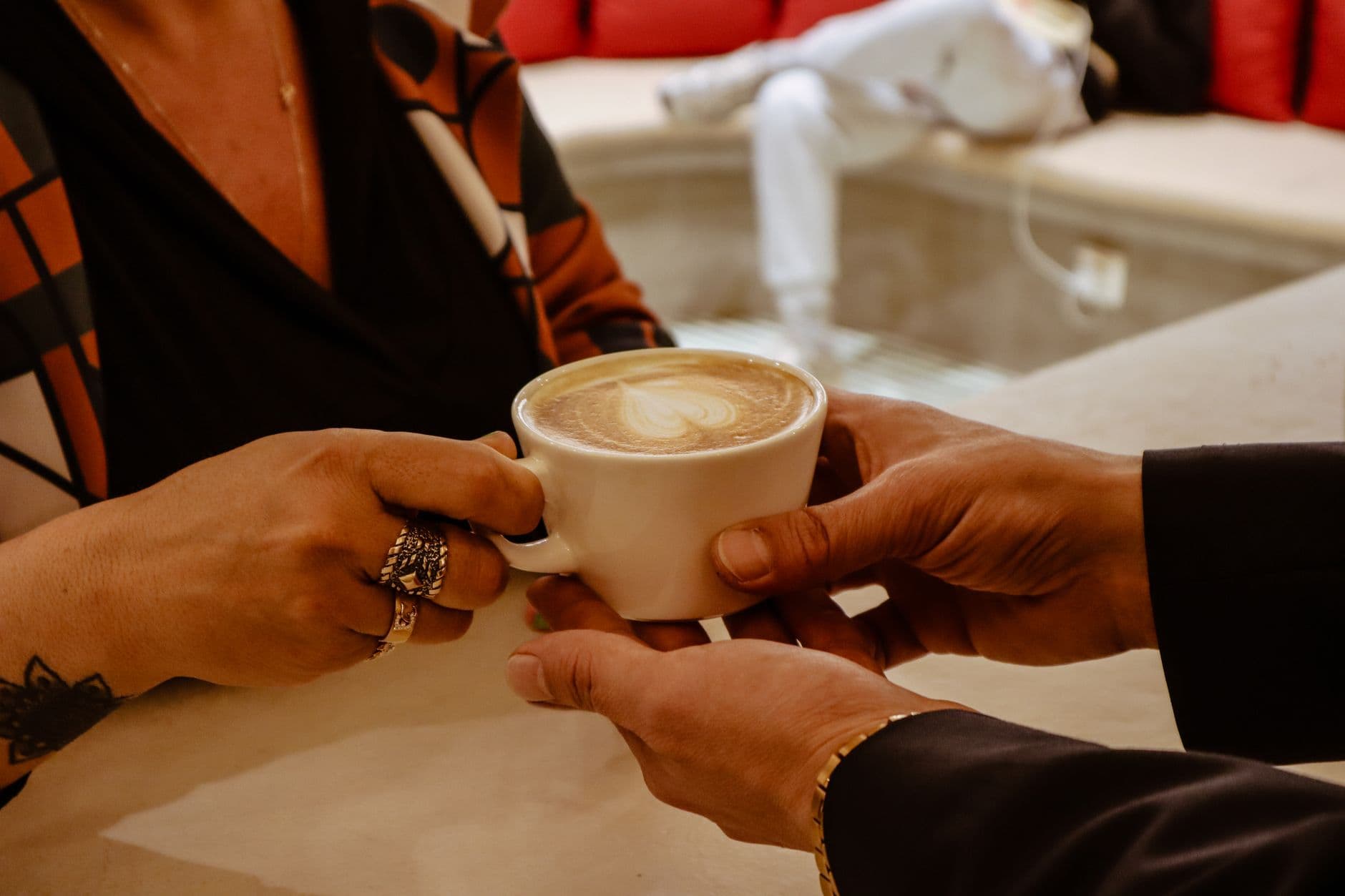 Close-up of hands exchanging a latte with intricate art in a cozy café setting.