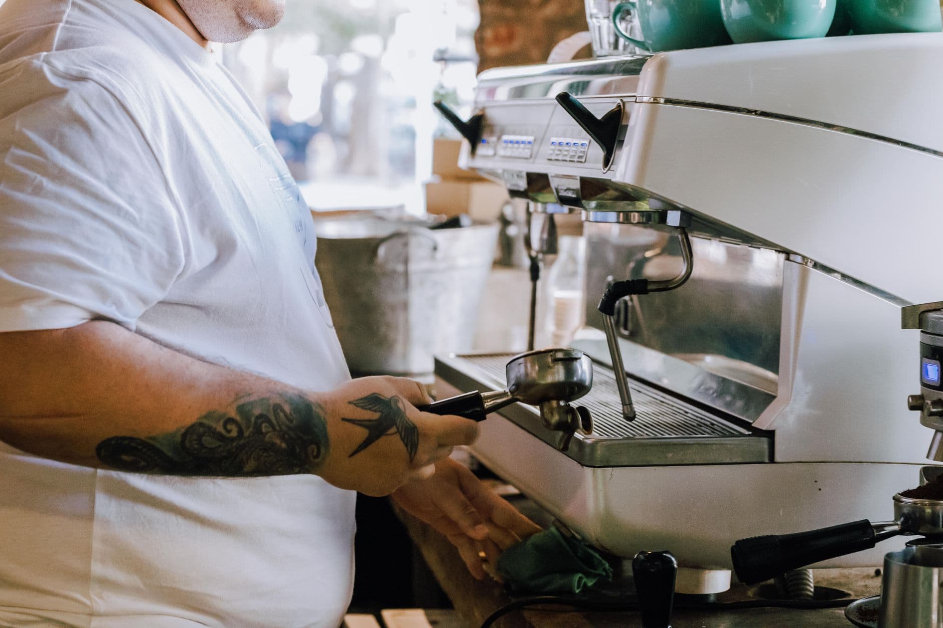 Barista making coffee with espresso machine in Buenos Aires café. Close-up of tattooed arm and coffee preparation.