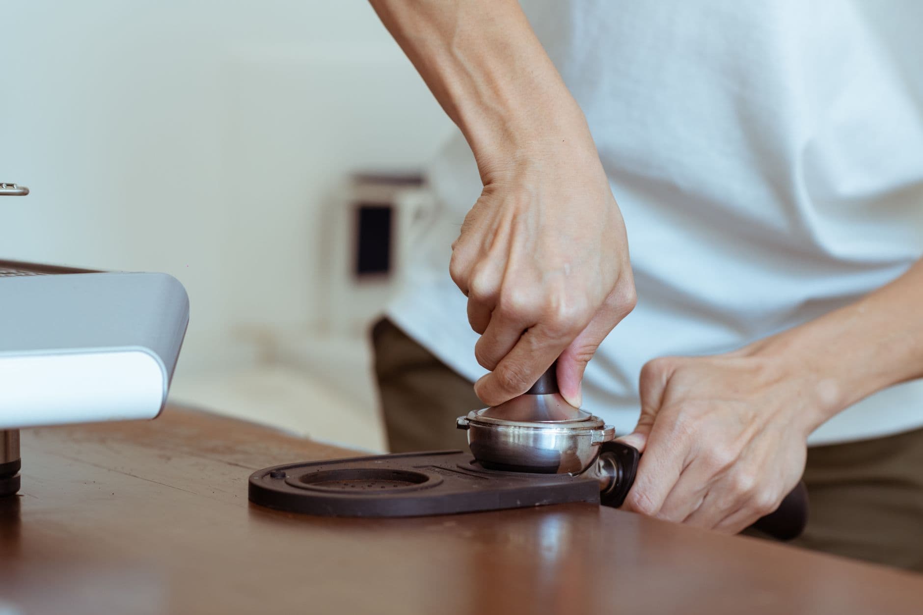 Crop anonymous cafe employee in white tee using tamper to press freshly ground morning coffee in portafilter