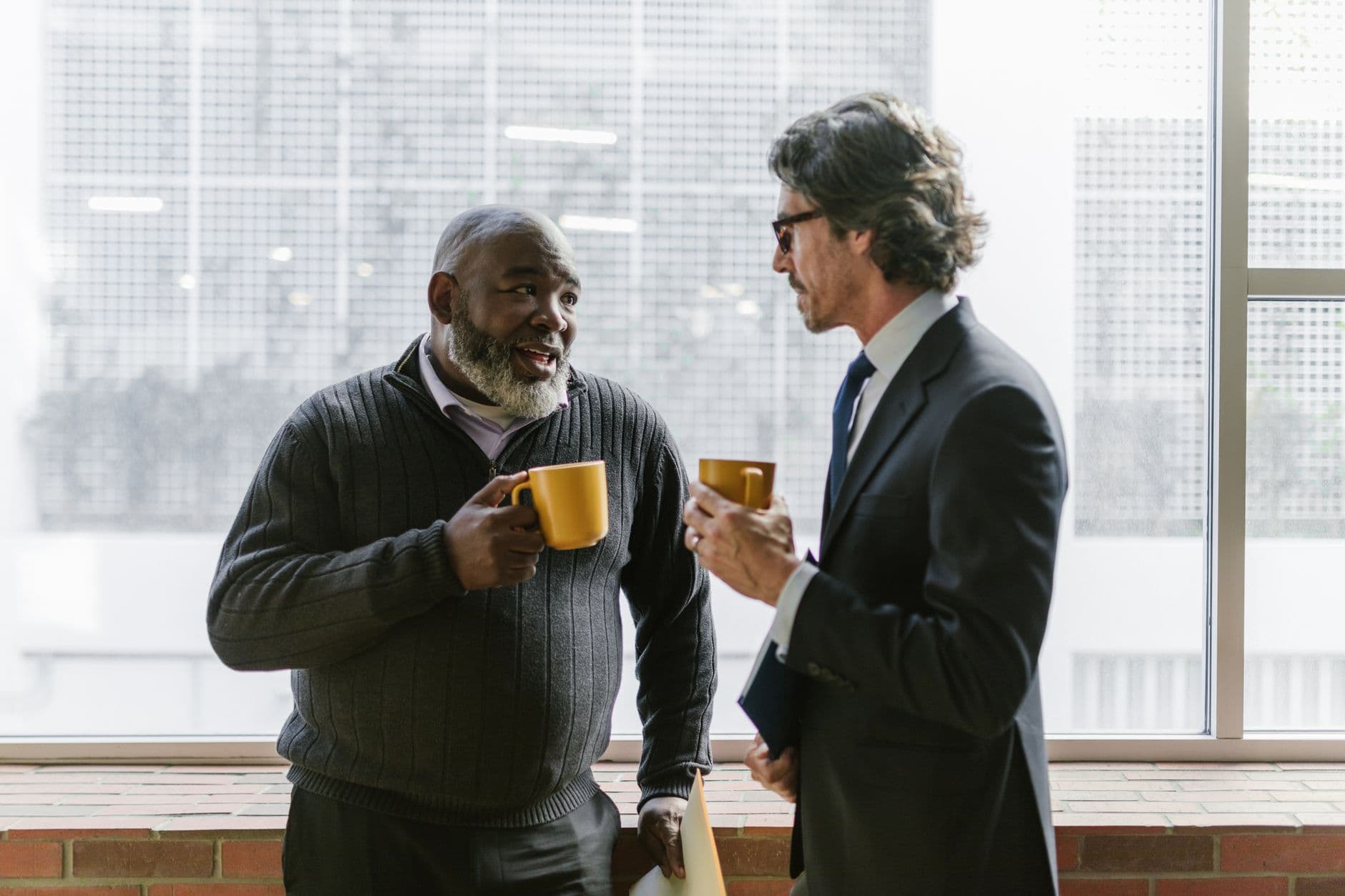 Two senior businessmen in conversation, enjoying coffee in a bright office space.