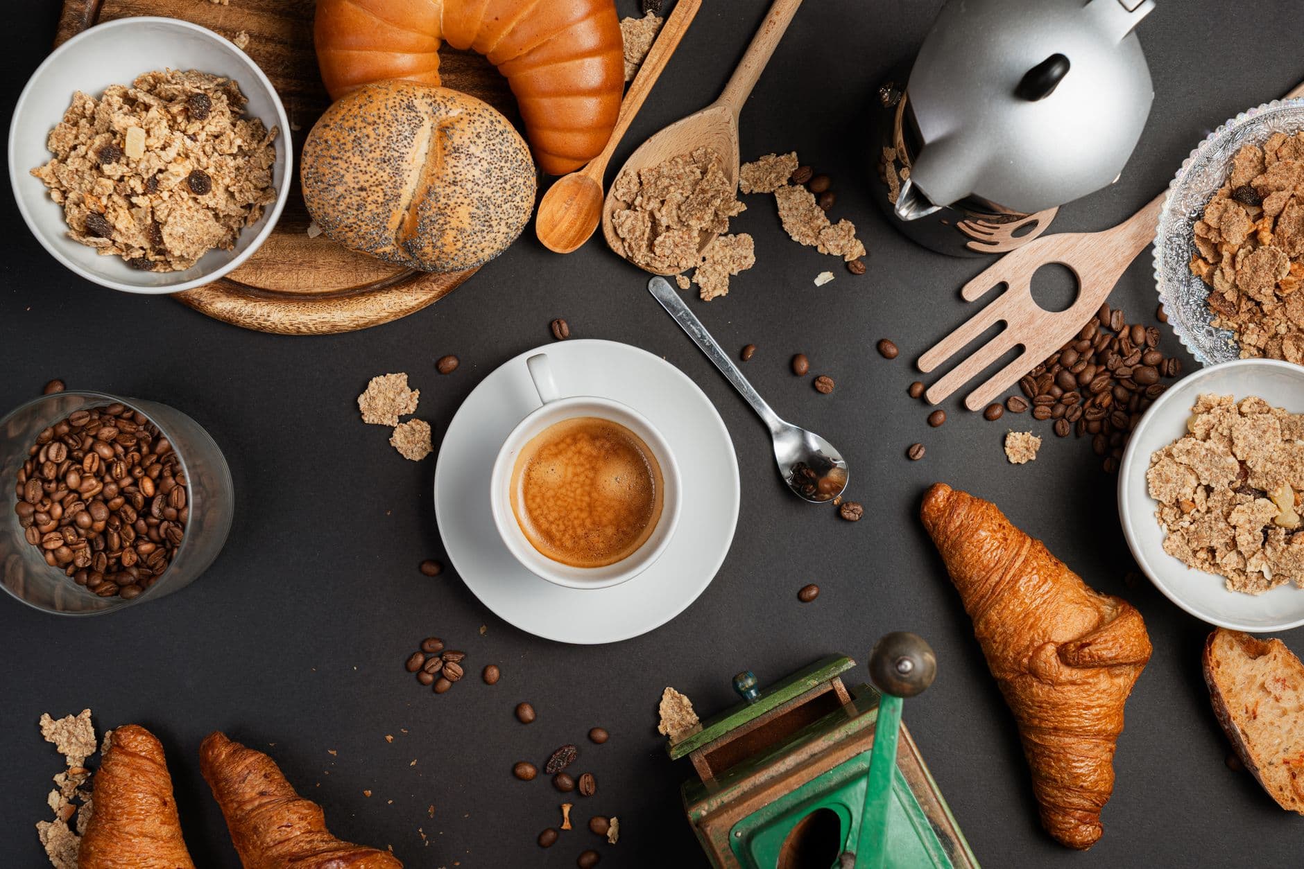Flat lay showcasing an espresso cup, croissants, bread, coffee beans, and cereal for a cozy breakfast vibe.