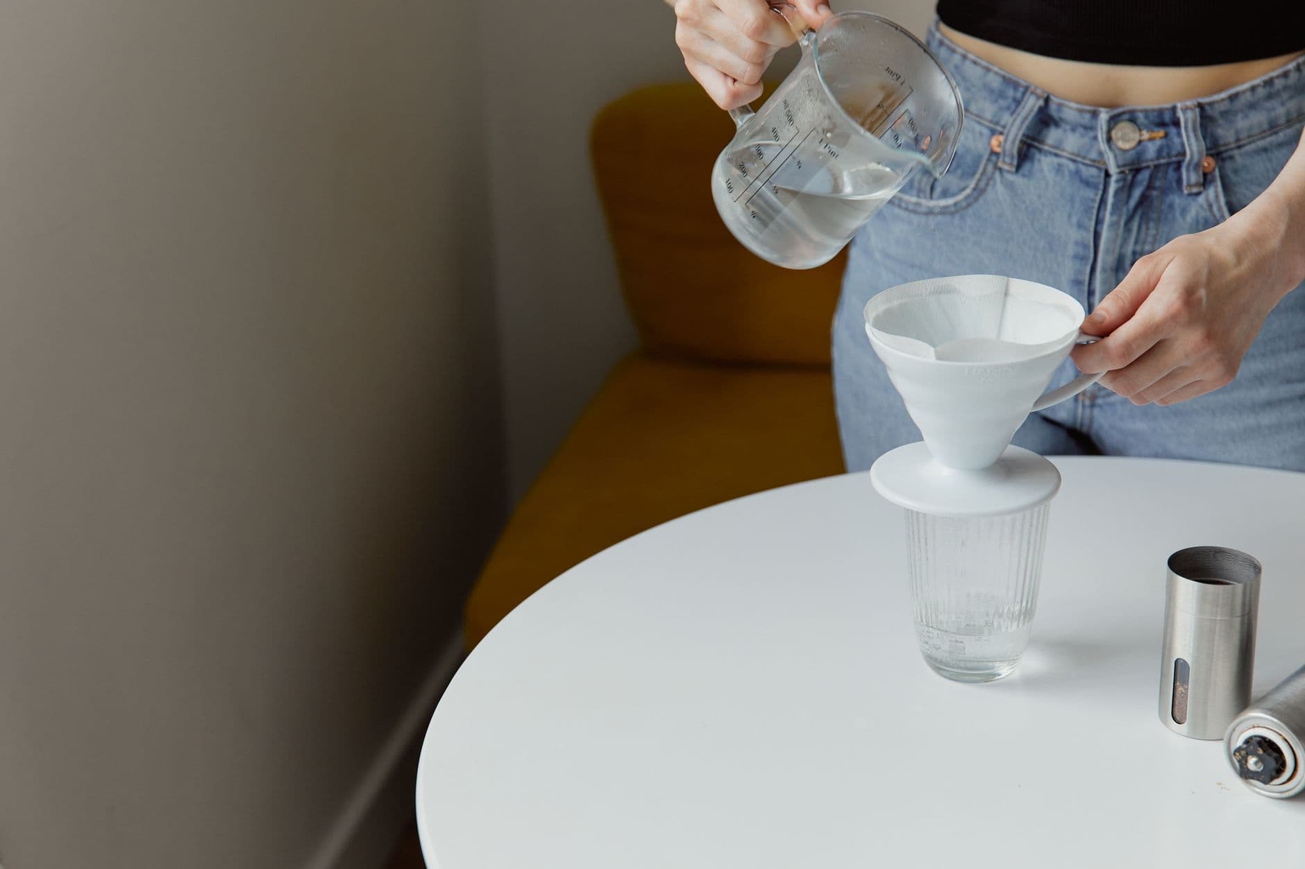 A person preparing pour-over coffee with a glass kettle and paper filter indoors.