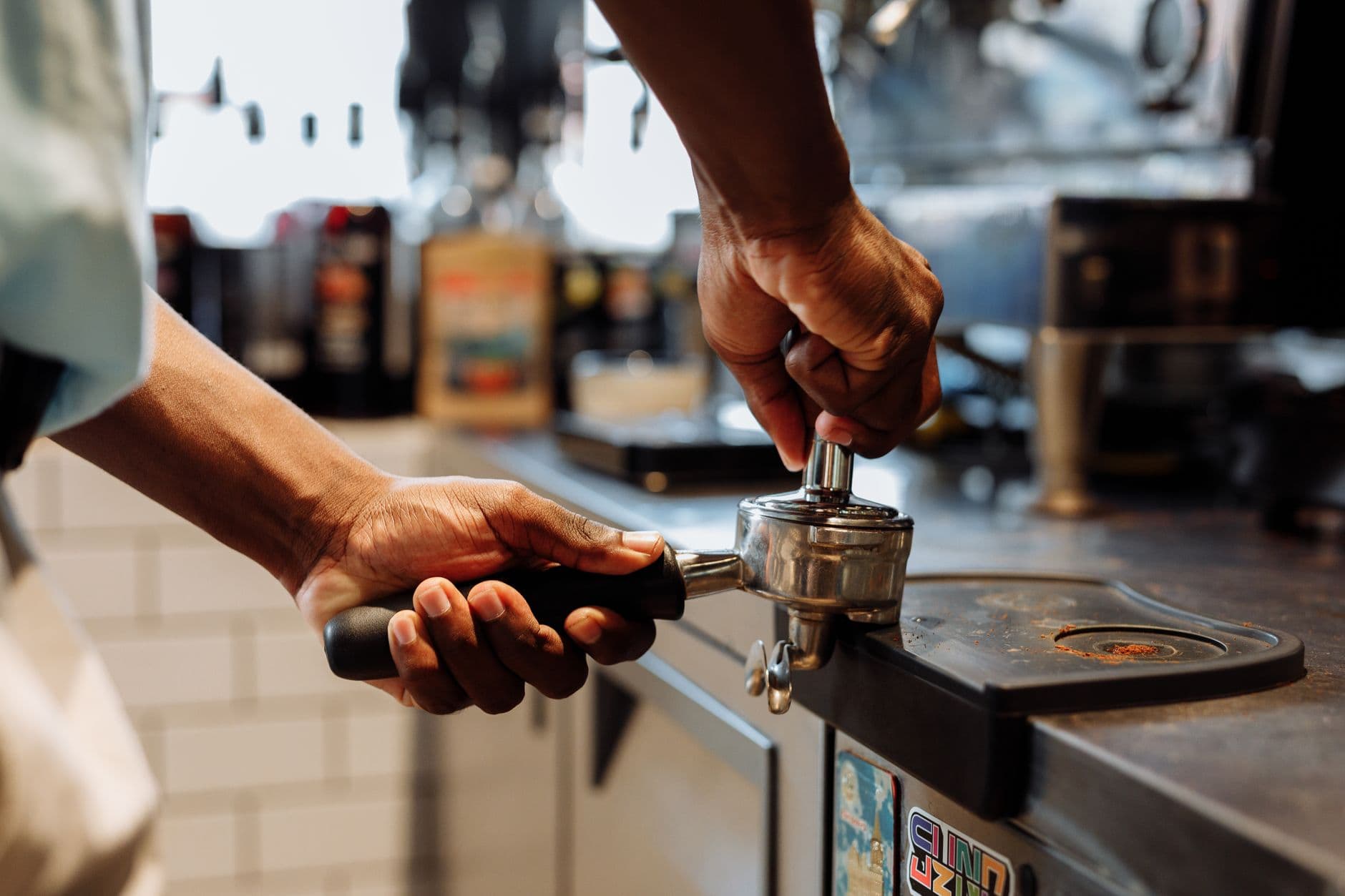 Close-up of a barista using a tamper on a portafilter in a coffee shop setting.