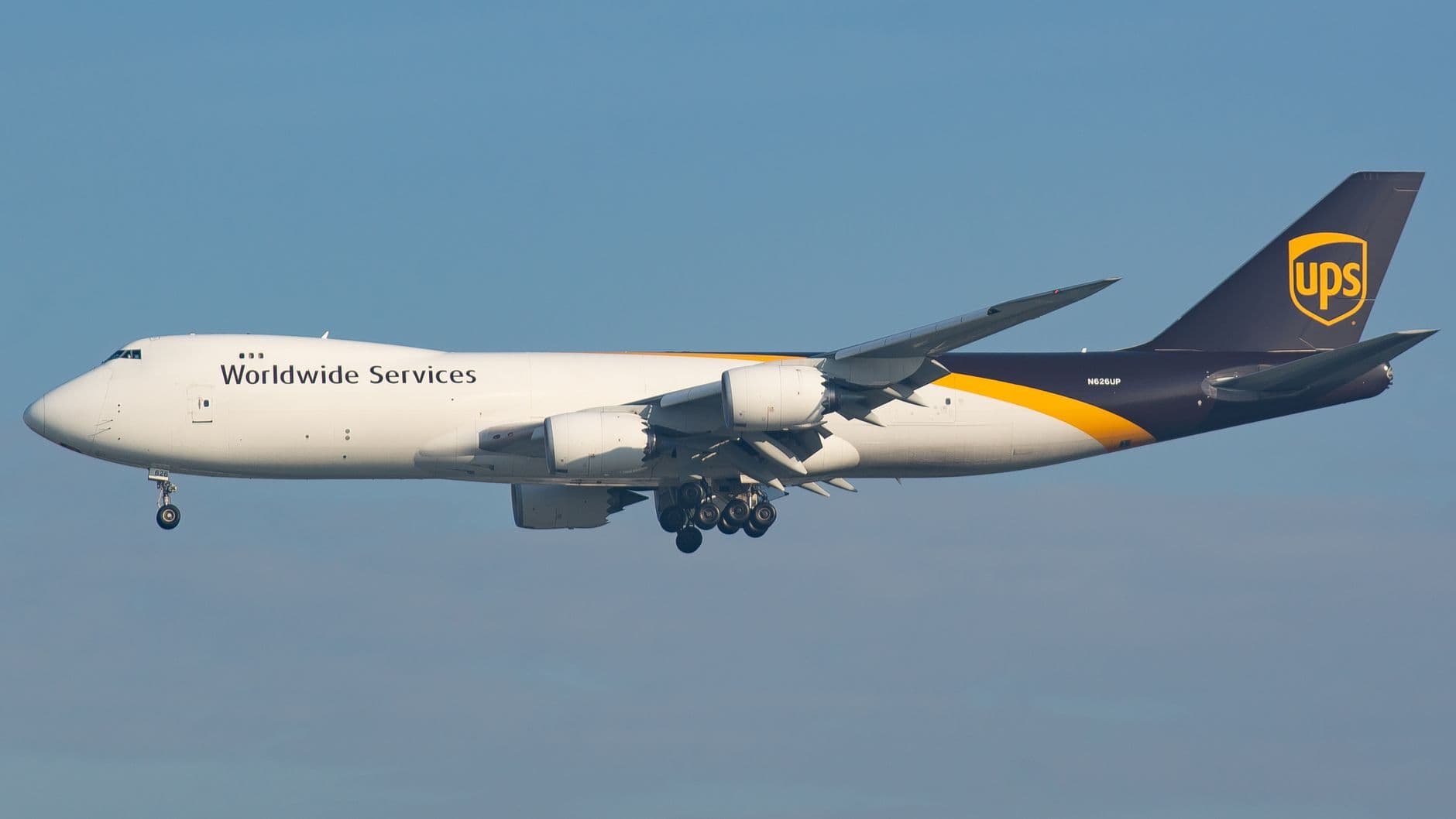 UPS cargo plane in flight against clear blue sky, showcasing delivery services.