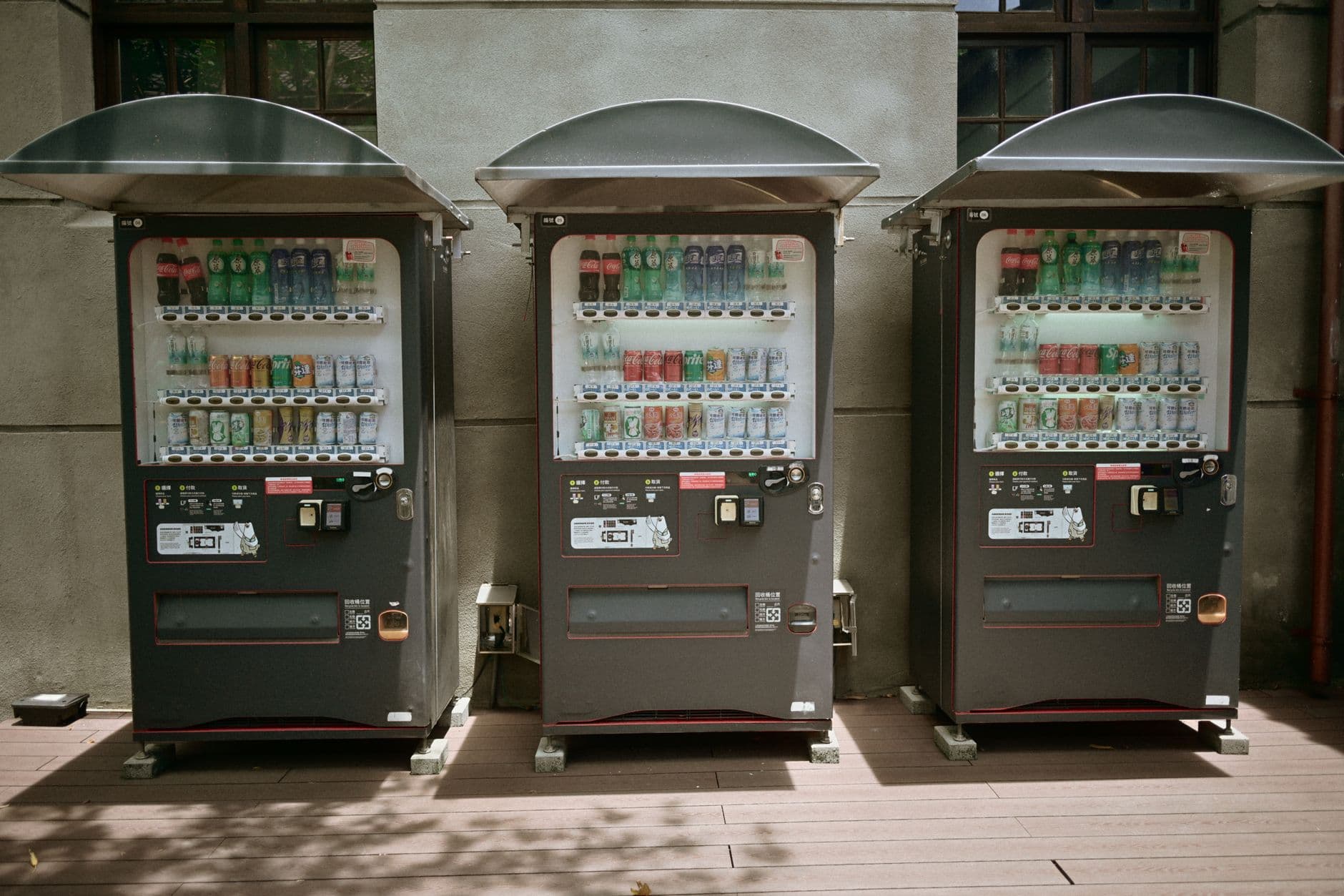 Three vending machines filled with drinks sit outdoors in Taiwan.