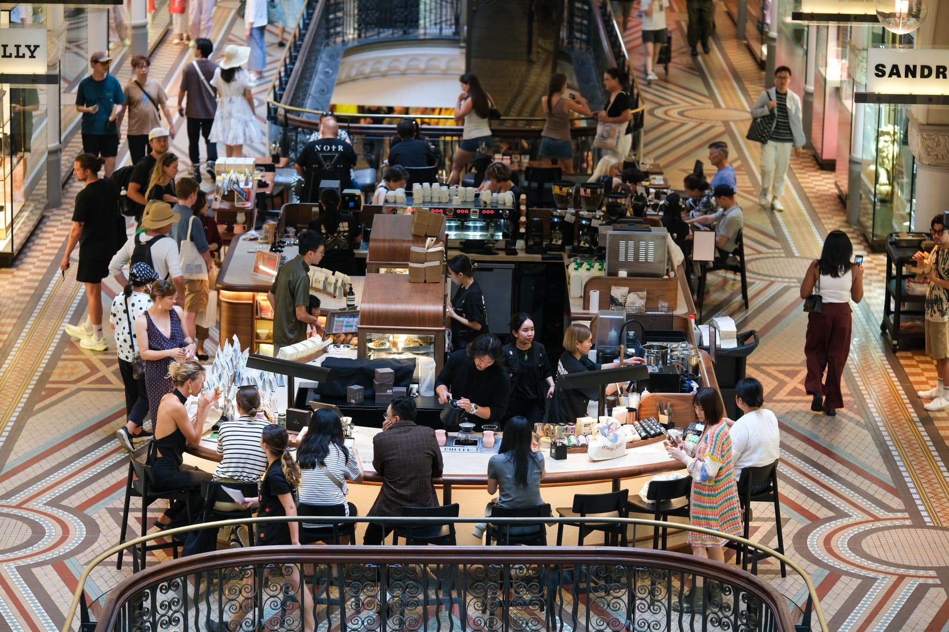 A bustling coffee shop inside a high-end shopping mall filled with diverse visitors and elegant decor.