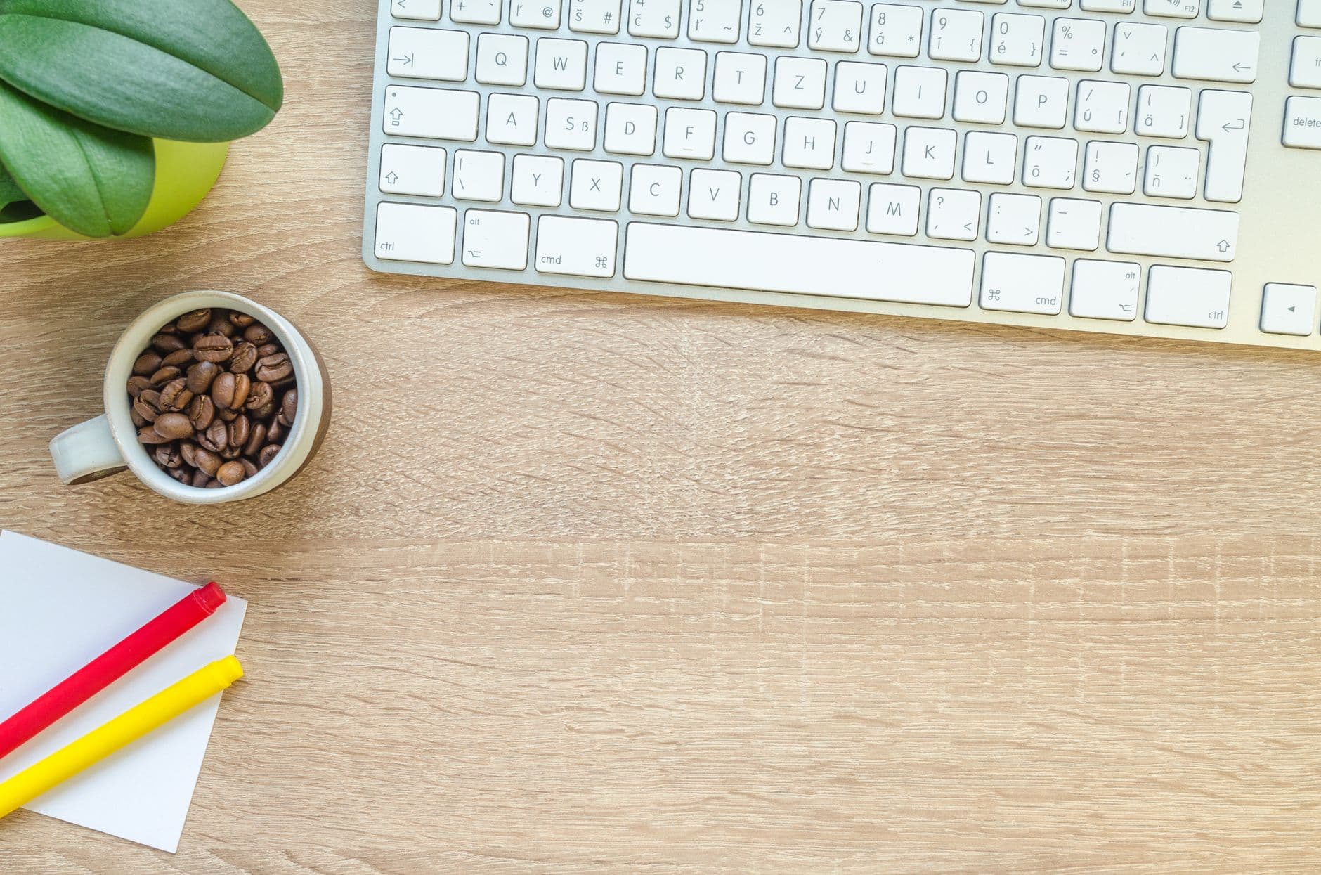 Overhead view of keyboard, coffee beans, and stationery on a wooden desk.