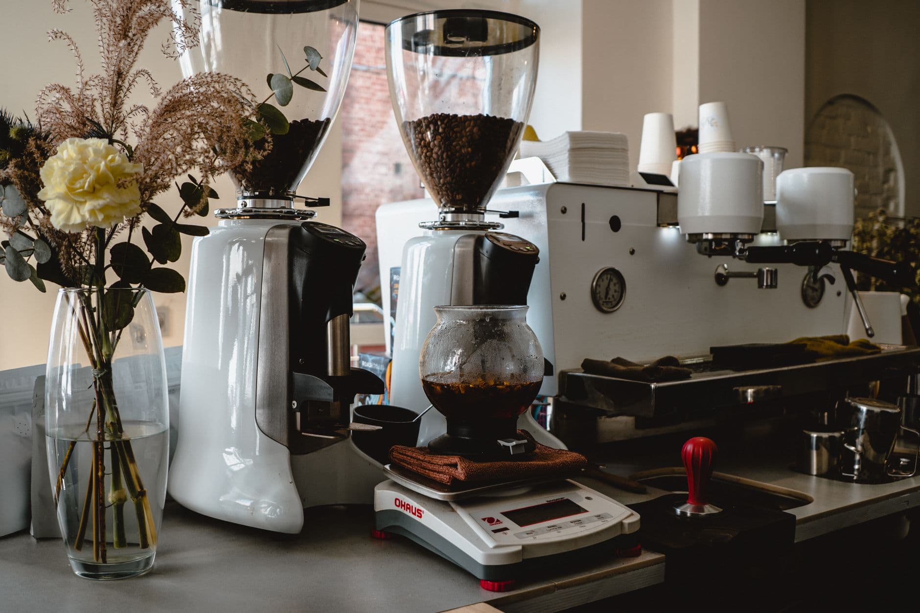 A cozy coffee shop setup with grinders, coffee machines, and decorative flowers.