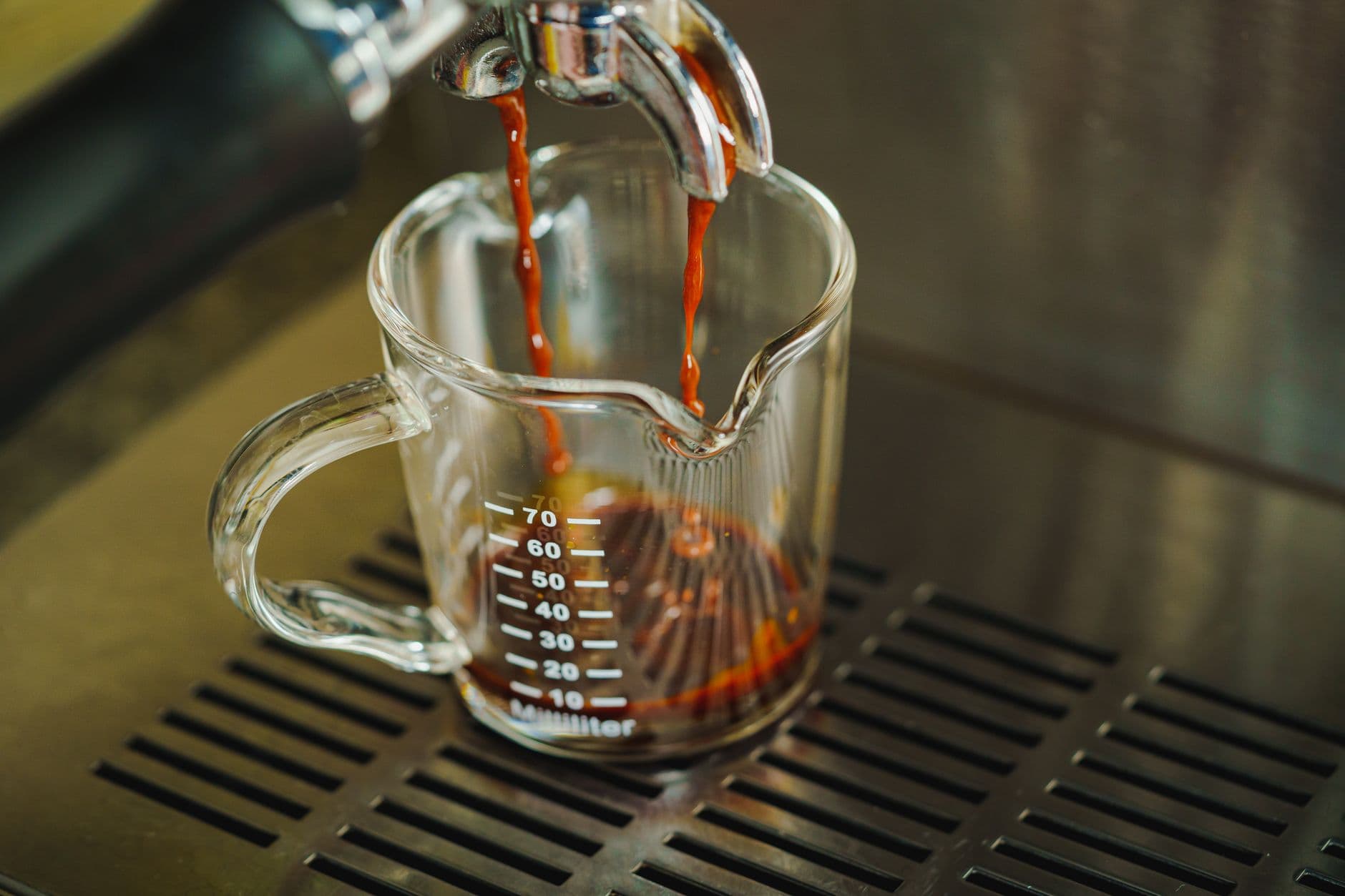 Fresh espresso shot being poured into a glass measuring cup on a coffeemaker.