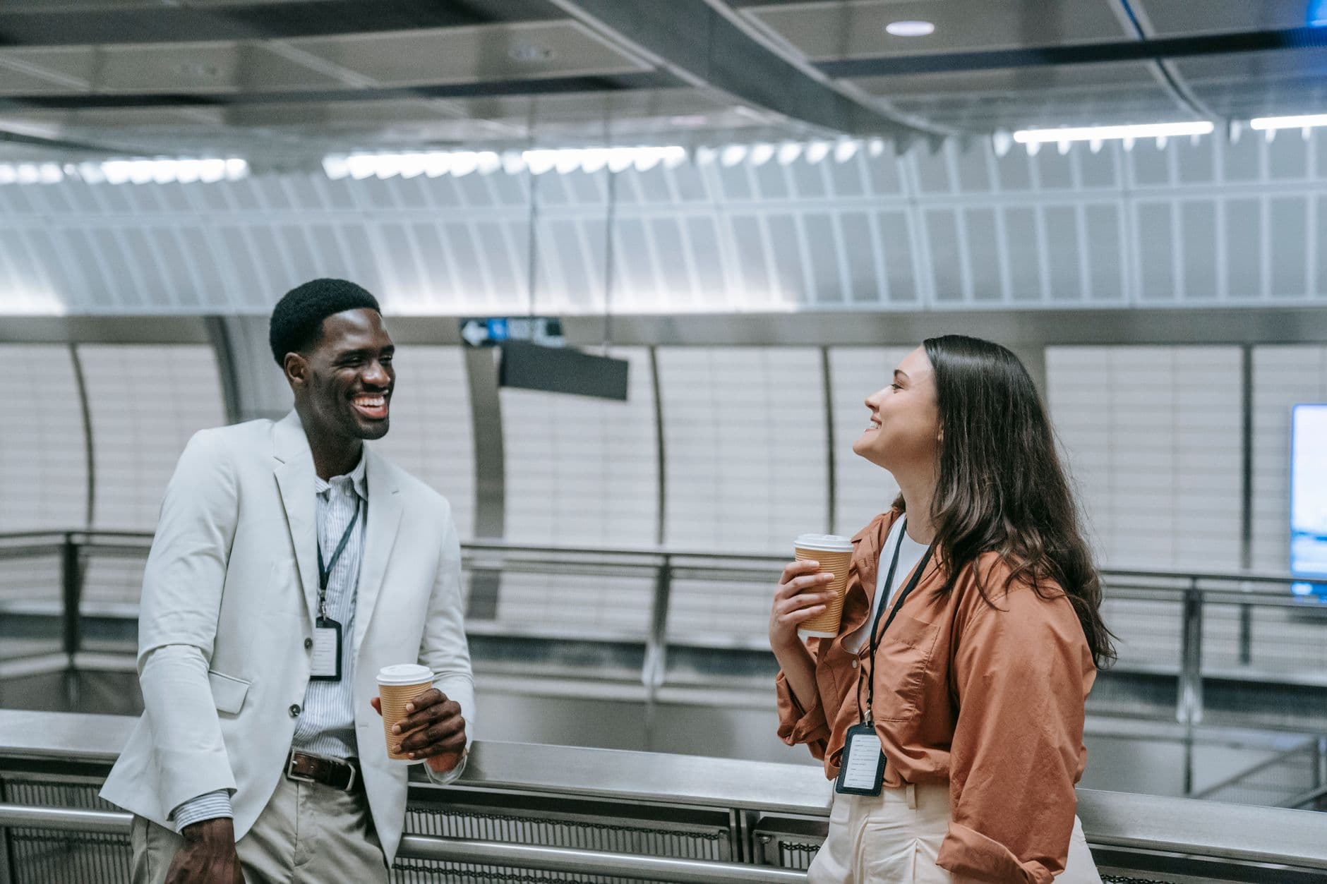 Two professionals chat warmly over coffee in a sleek, modern building setting.