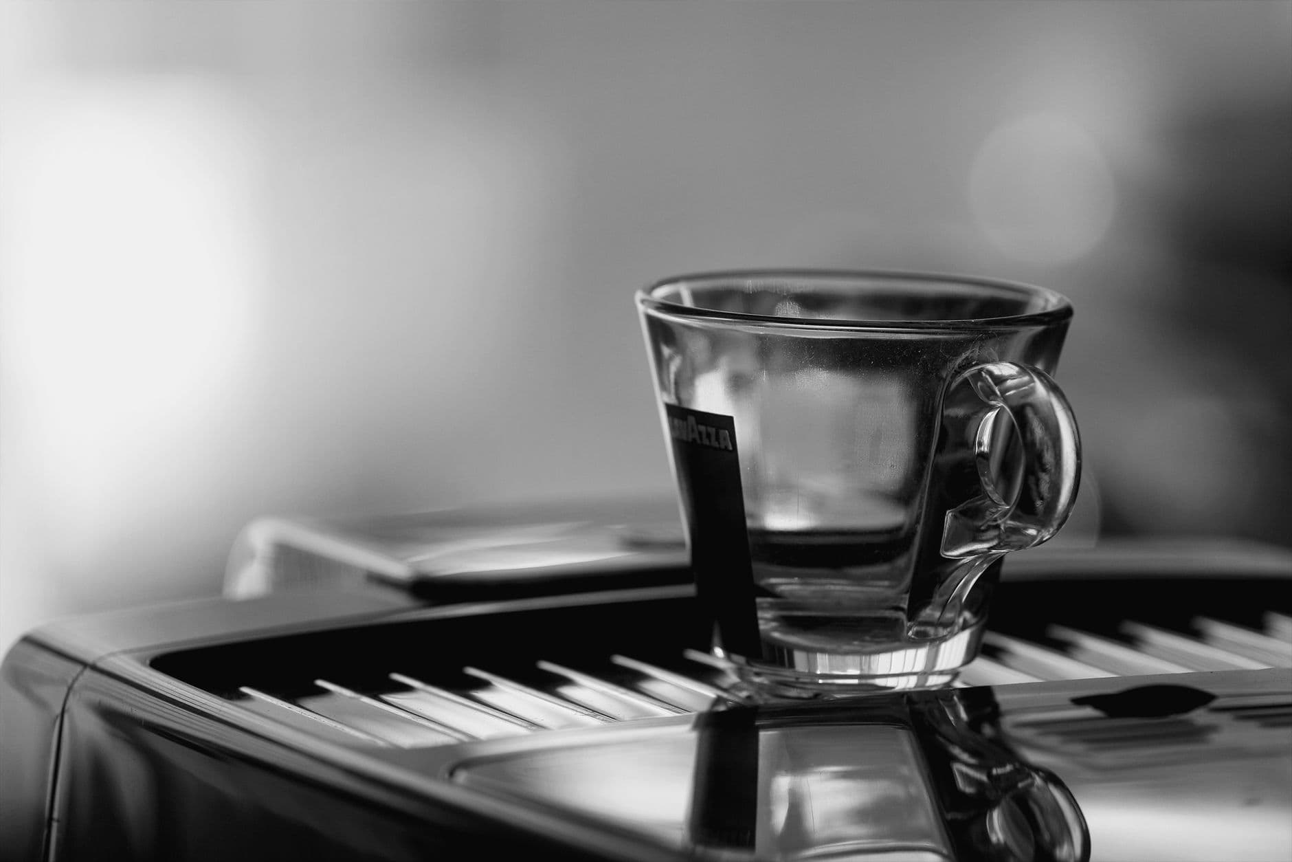 A clear glass espresso cup on a modern coffee machine in black and white.