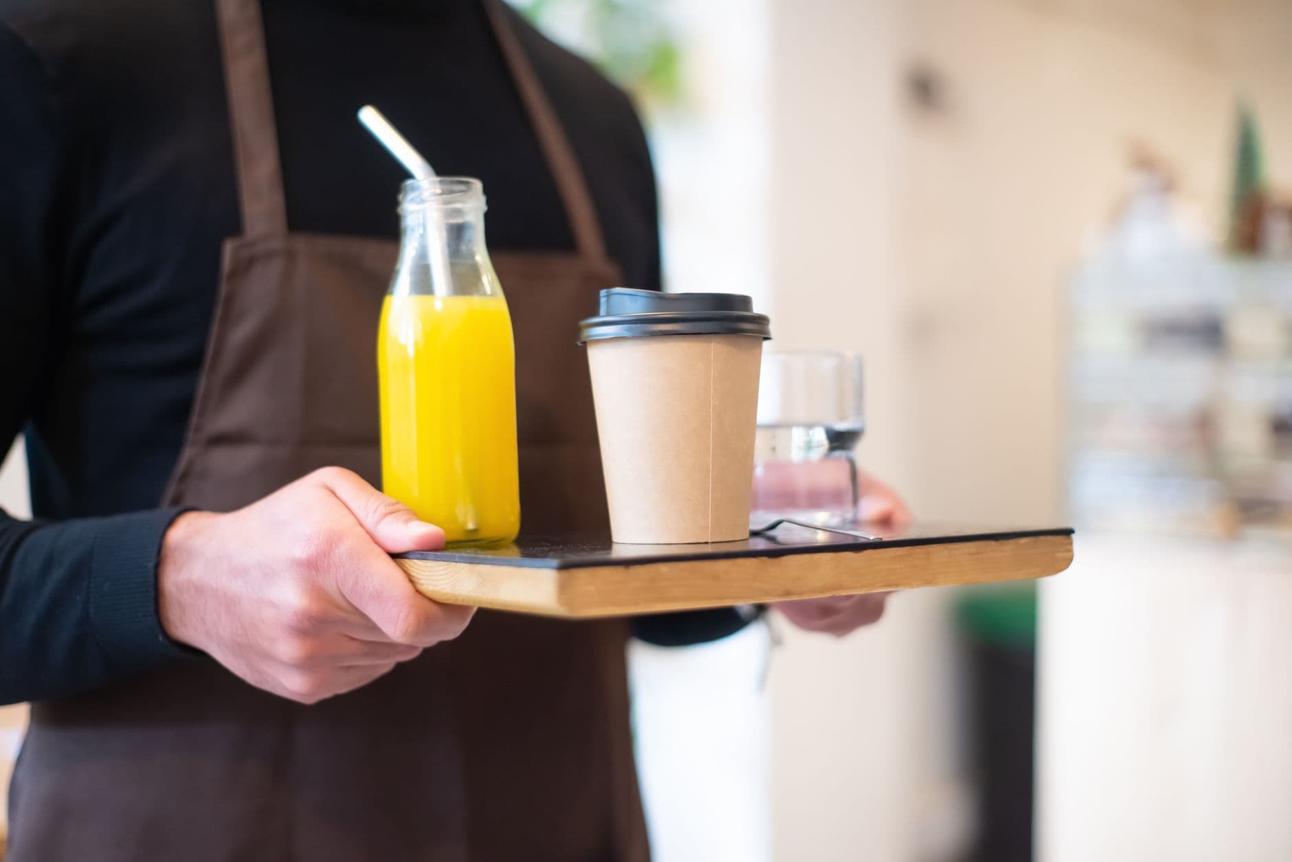 A barista serves juice and coffee on a wooden tray in a cozy café setting.