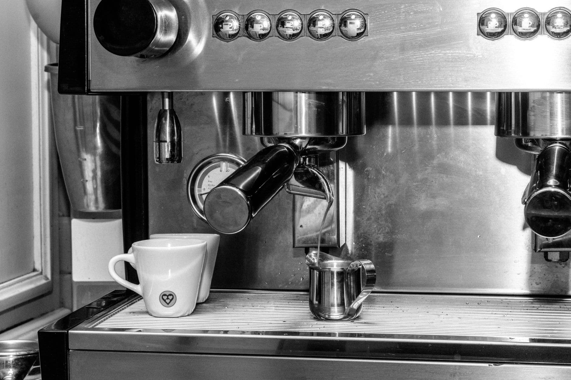 Black and white close-up of an espresso machine with a cup and milk frother.