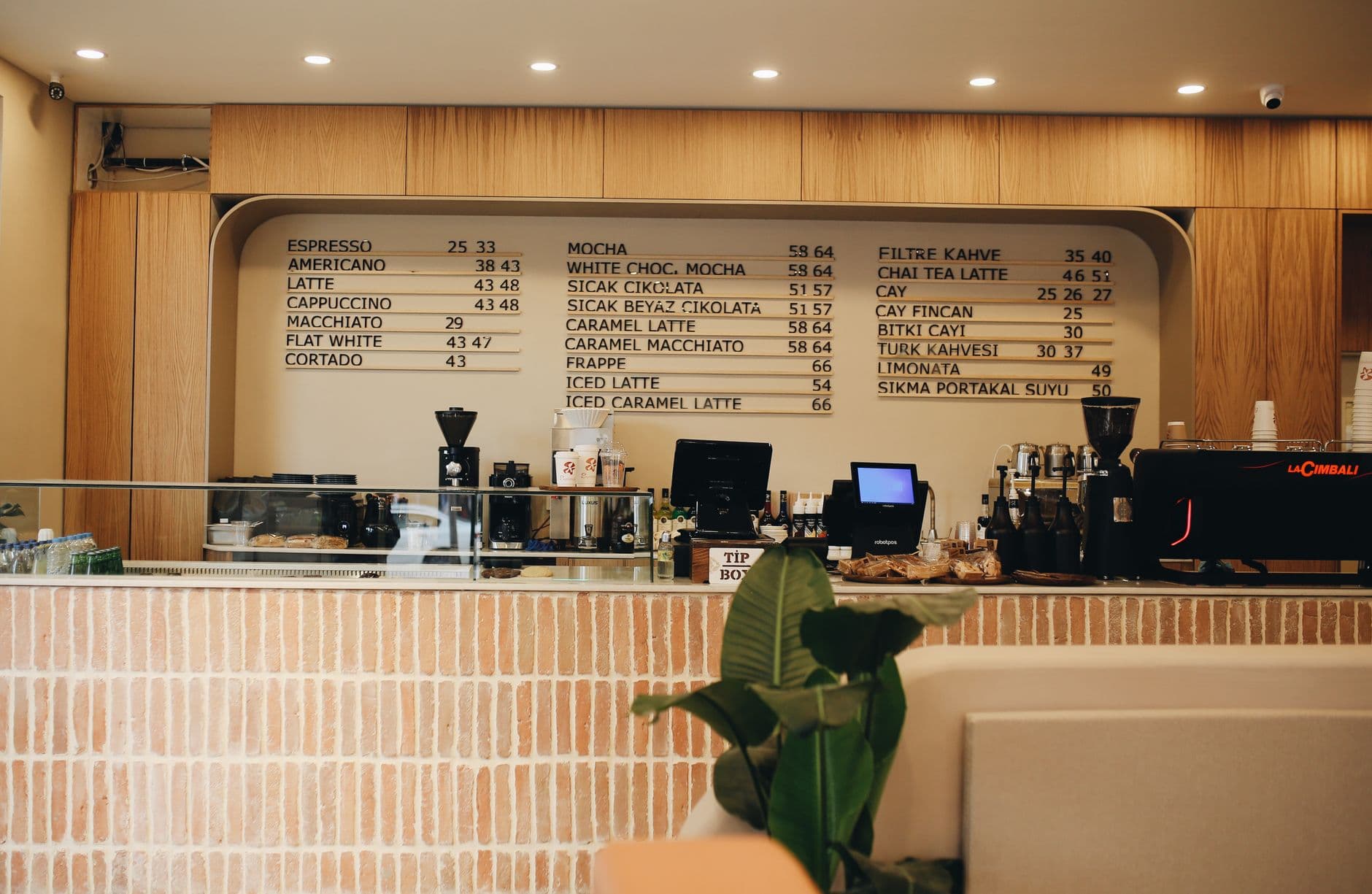 Warm café interior featuring a detailed coffee menu and counter setup with plants.