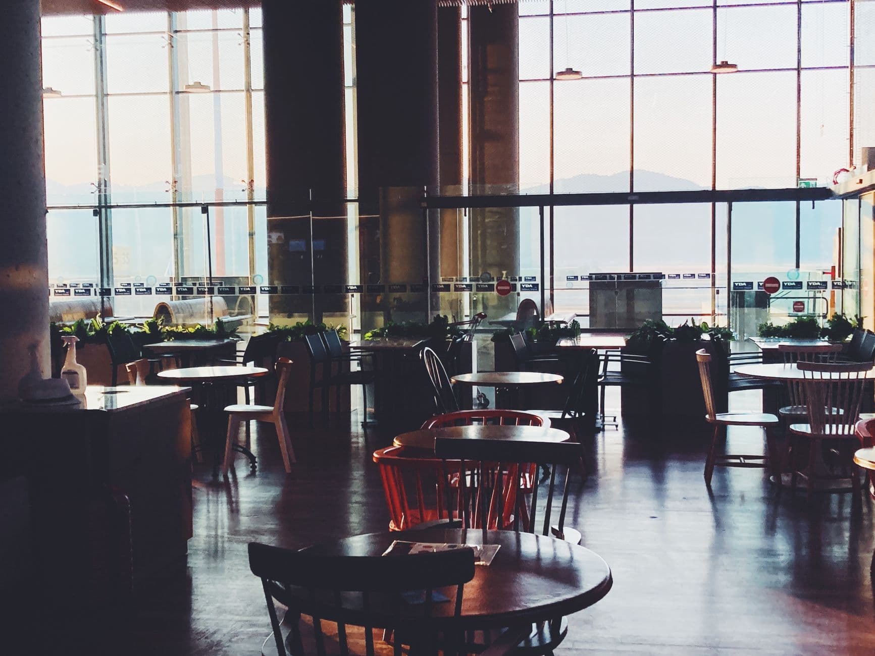 A quiet modern cafe interior with round tables and chairs, offering panoramic views through large windows.