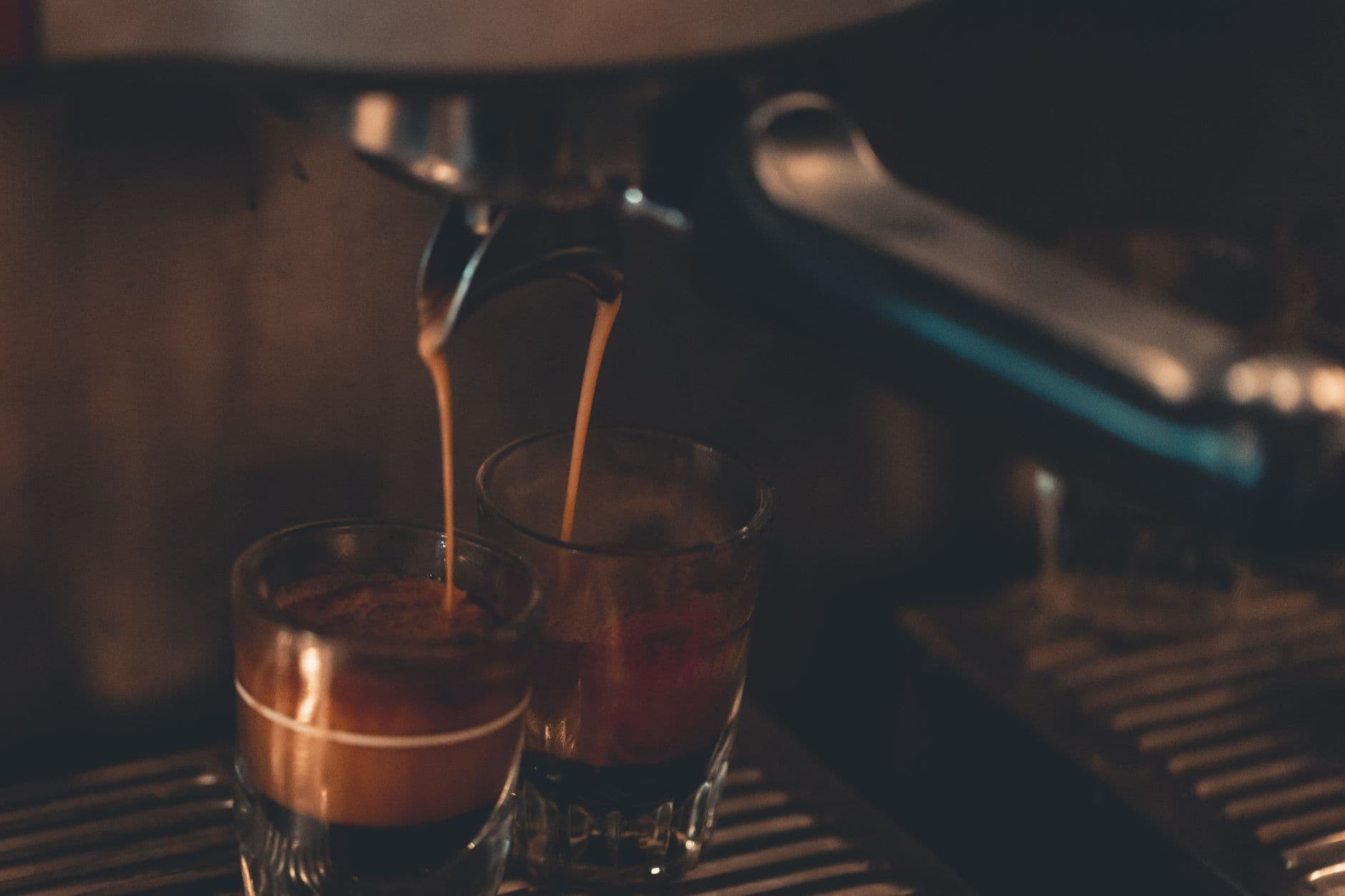 Close-up view of hot espresso pouring into two glasses, creating a rich coffee aroma indoors.