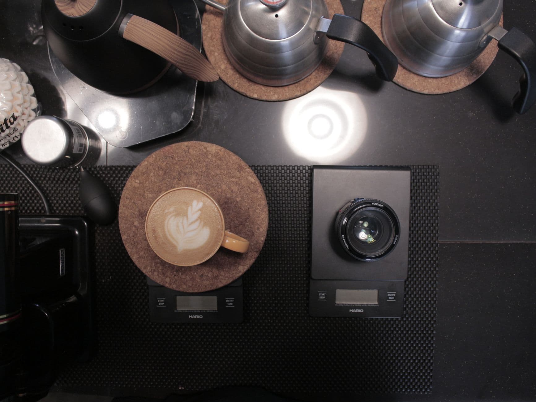 Top view of a latte on a scale and camera lens on a black table in Bandung cafe.
