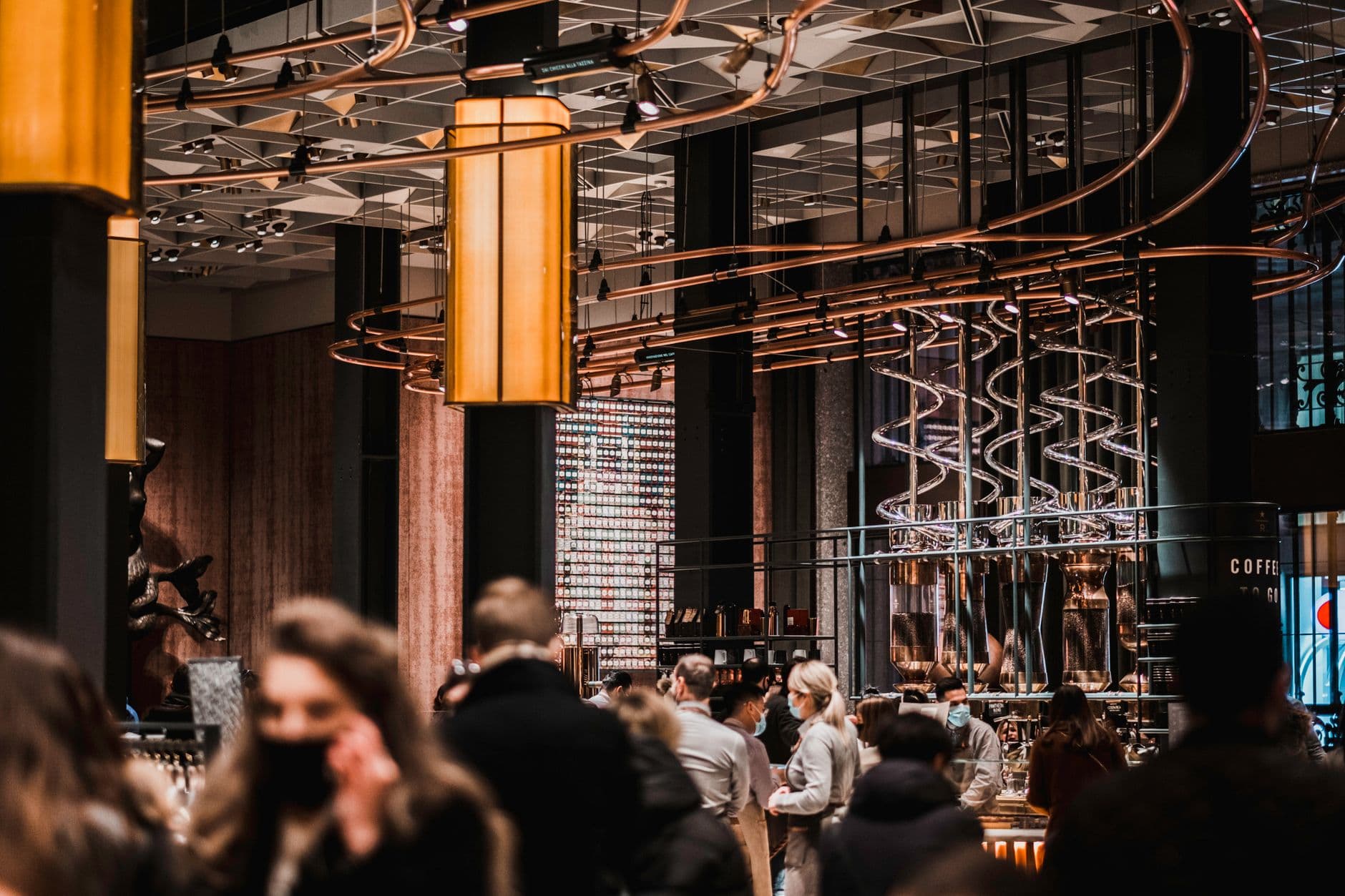 A busy coffee shop interior showcasing modern design with people wearing masks, reflecting the new normal.