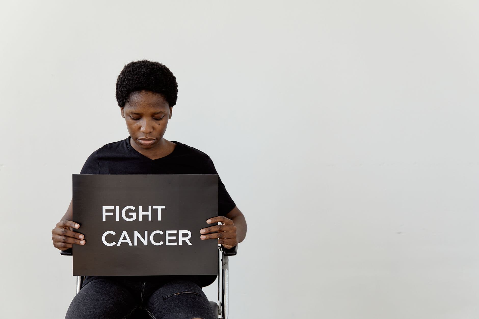 A woman holds a sign that reads 'Fight Cancer' in a studio setting with a minimalist look.